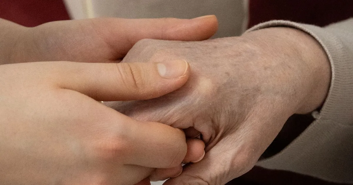 A younger hand gently cradles an older parent's hand in a warm, reassuring gesture of support
